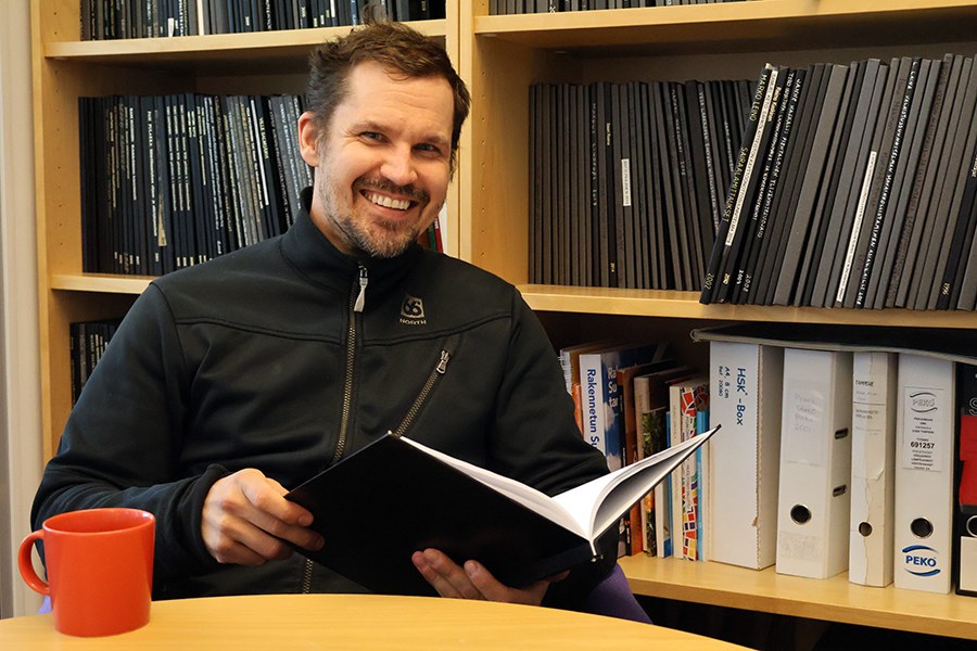 Mies lehteilee opinnäytetyötä kirjahyllyn edessä. 