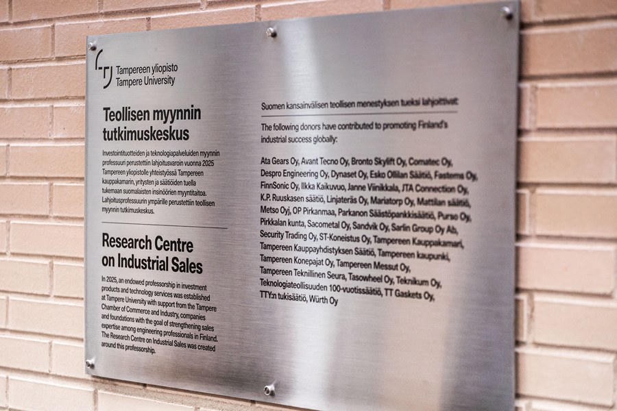 Tiiliseinään kiinnitetty kiiltävä taulu, joka sisältää tekstiä.