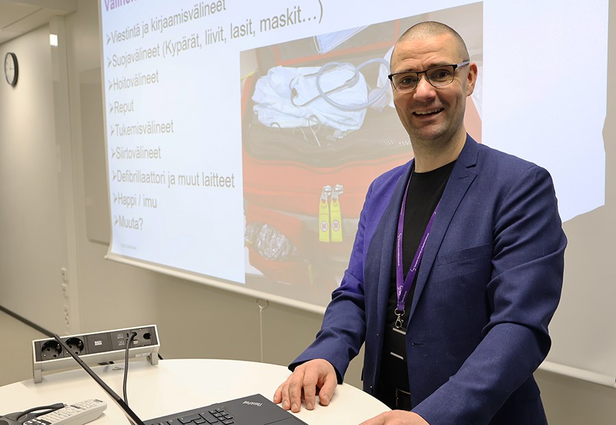 Puvun takkiin pukeutunut mies opettaa luokassa. 