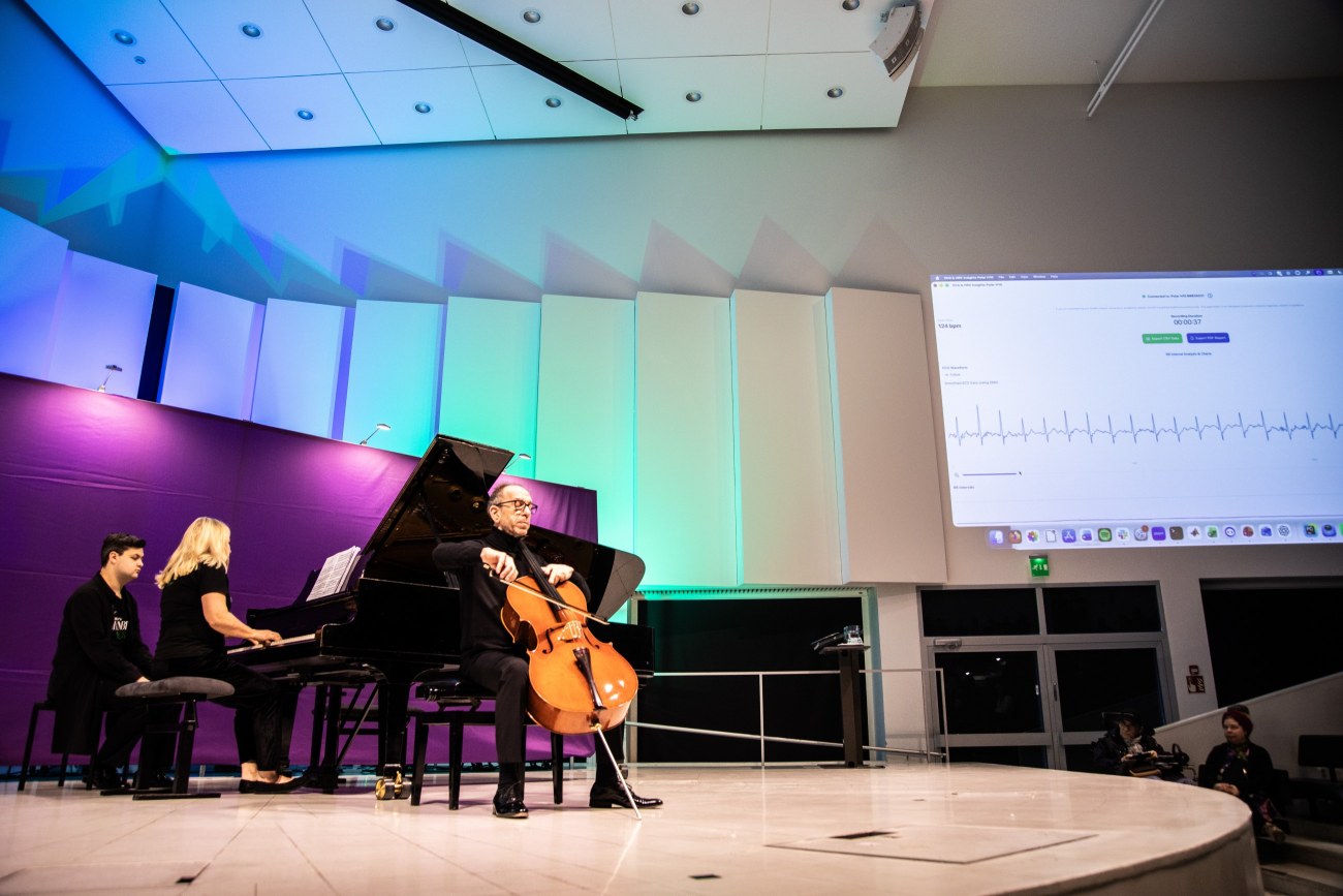 Sellisti soittaa keskellä esiintymislavaa, ja hänen takanaan pianisti soittaa flyygeliä. Taustalla on sykekäyrä, joka on projisoitu juhlasalin seinälle.