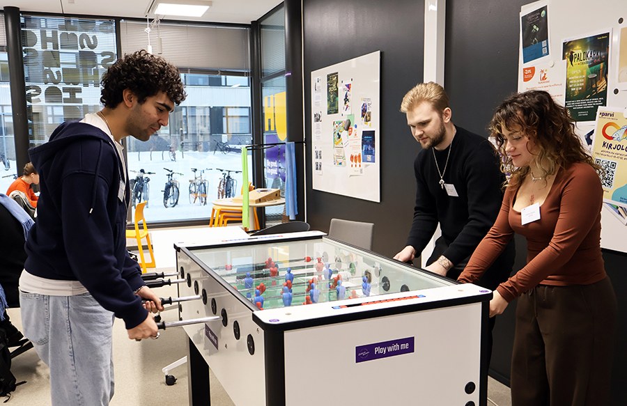 Kolme nuorta aikuista pelaamassa pöytäjääkiekkoa.