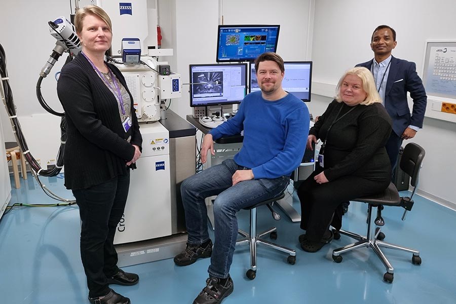 Kolme henkilöä poseeraa läpivalaisumikroskoopin vierellä.