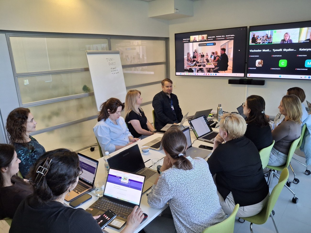 Student and staff seated around a table with online participants visible on the screens