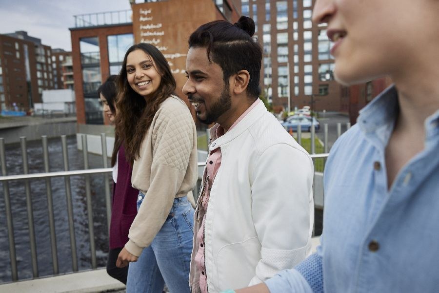 A group of happy international students walking by the channel, behind them red apartment buildings.