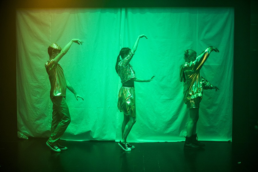 Kolme näyttelijää tanssivat vihreässä valaistuksessa. Taustalla kangas.